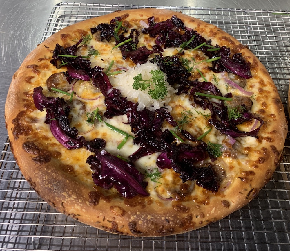 this photo shows the pizza with strips of red cabbage laid over the crust, a heap of sauerkraut in the middle and parsley garnishes sprinkled throughout for additional color
