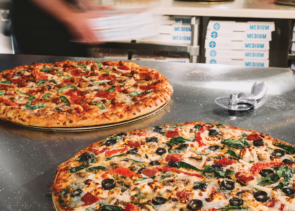 this photo shows two different specialty pizzas from Domino's with delivery/carryout boxes blurred in the background