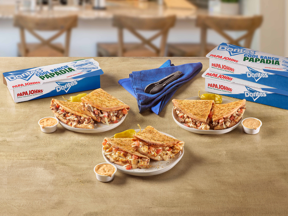 this photo shows several versions of the Doritos Cool Ranch Papadia on a table along with carryout containers branded with both Papa Johns and Doritos logos