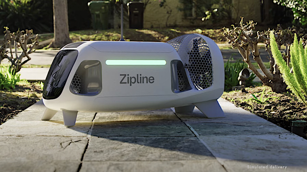 this photo shows a Zipline drone, a small, white, bus-shaped machine, perched on a sidewalk