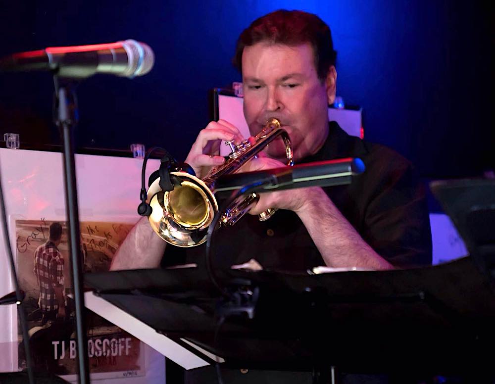 this photo shows Jeff Dodge playing his trumpet in a dark setting that appears to be a club or a bar