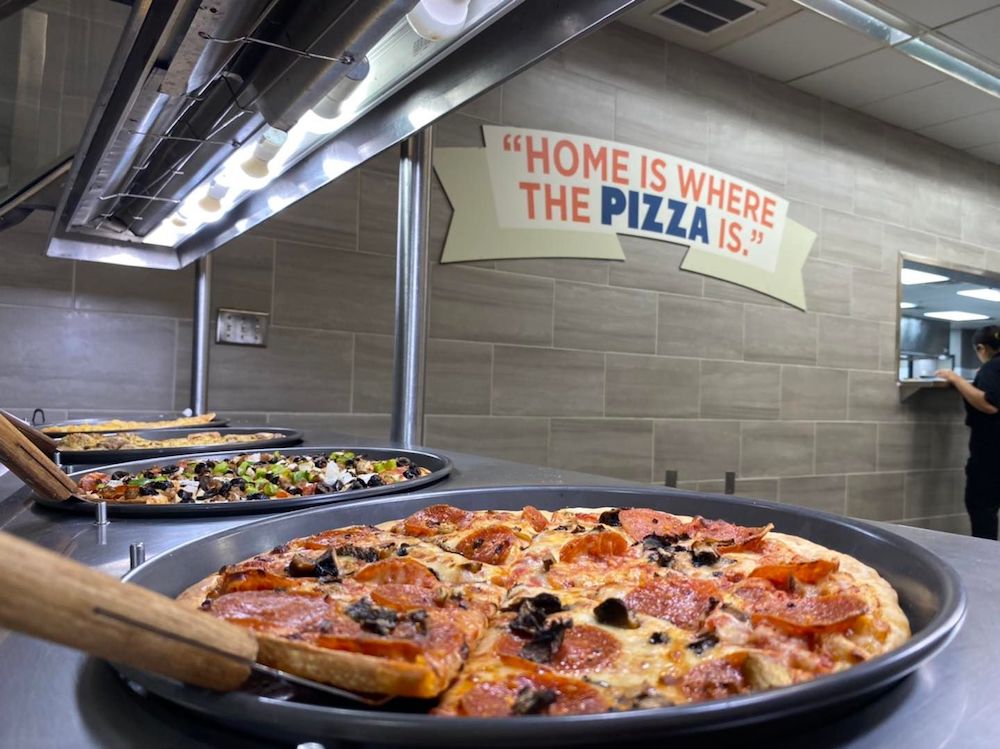 this photo shows a Mr Gatti's buffet station with several pizzas and, in the background, a sign that reads, Home is where the pizza is.