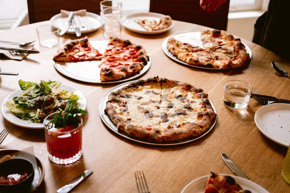 this photo shows several beautiful pizzas arrayed on a table, including the Cacio e Pepe pizza front and center, the Pepperoni pizza behind it along with the Smoky Eggplant pizza.