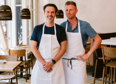 This photo shows the two co-chefs of Flour + Water standing side by side in their new restaurant, both men wearing aprons.