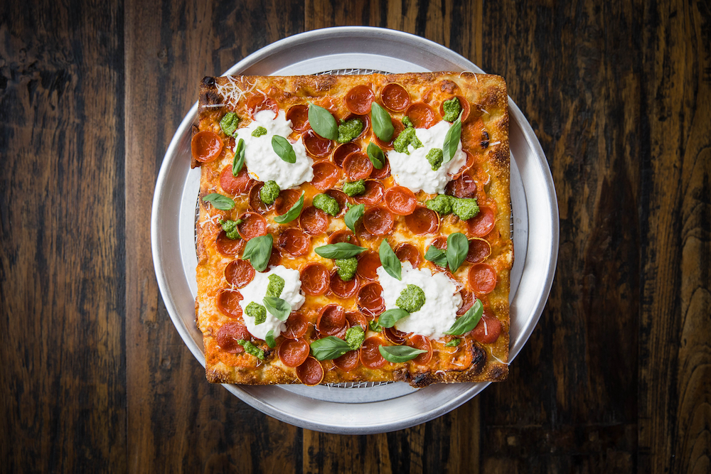 This photo shows a beautiful pizza topped with cup-and-char pepperoni and other ingredients against a black backdrop