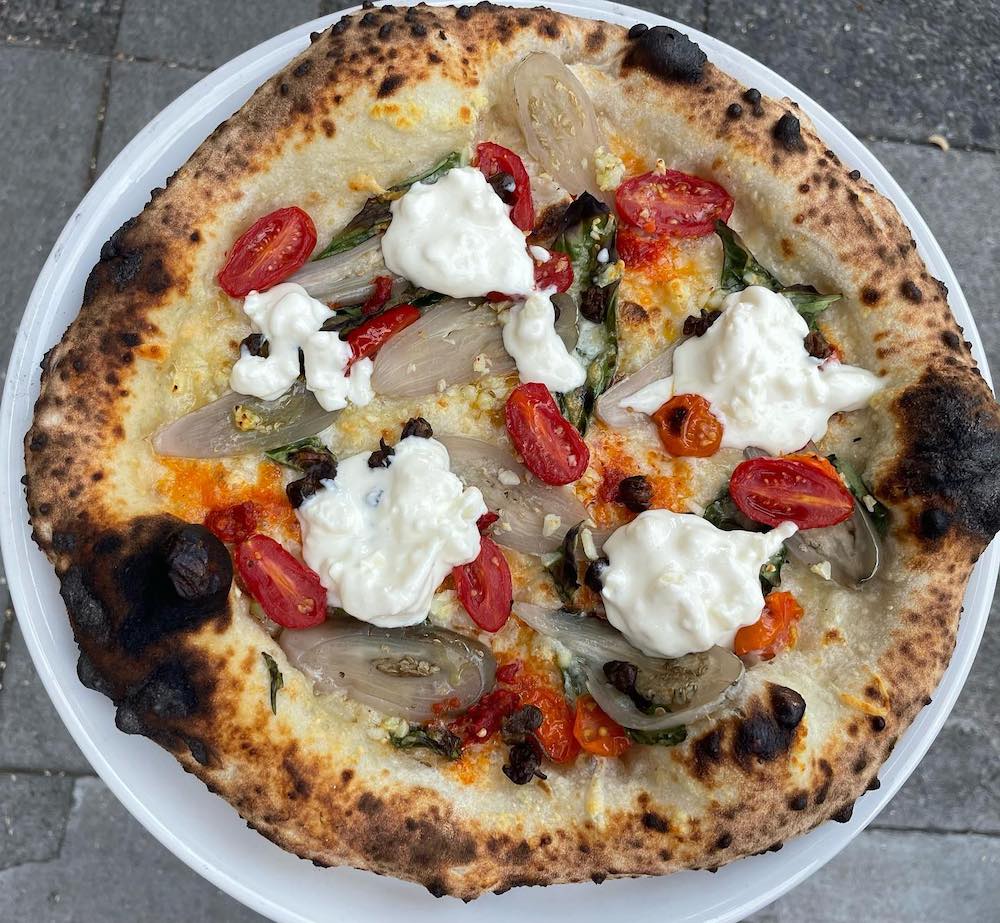 this photo shows a beautiful pizza in a white plate. It's topped with eggplant, tomatoes and stracciatella