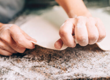 this photo shows a pair of hands stretching dough into a pizza crust