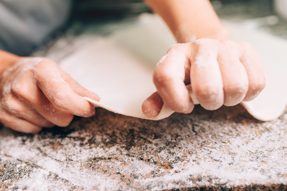 this photo shows a pair of hands stretching dough into a pizza crust