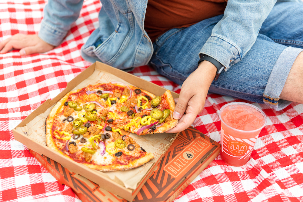 This photo shows a pizza from Blaze Pizza (in a box) topped with jalapeño peppers, yellow peppers, red onions and sausage