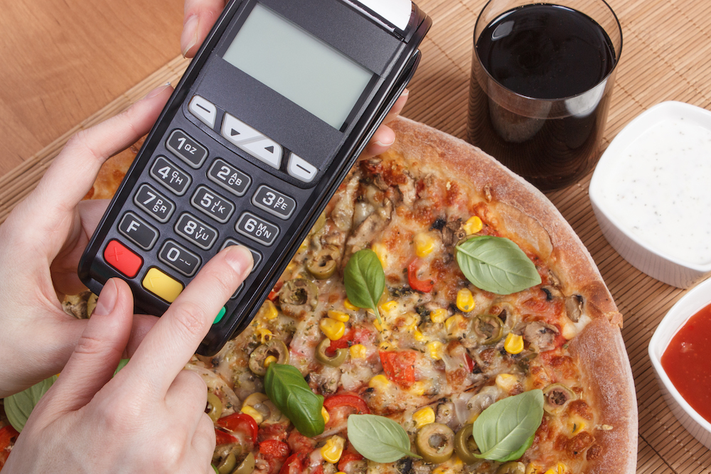 this photo shows a person using a credit card processing machine to pay for a pizza in a restaurant.