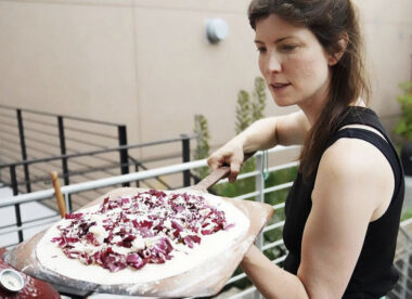 This photo shows Lauren Grimm, with long dark hair, getting ready to place a pizza into the oven.
