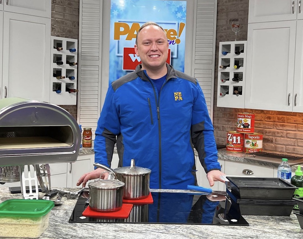 this photo shows a smilingJim Mirabelli in a blue jacket, standing in a kitchen set for the PA Live TV show