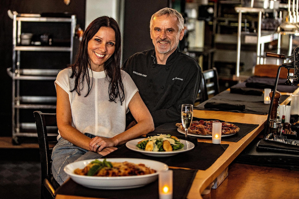 This photo shows a smiling Anita and Klime Kovaceski next to a counter laid out with several different artisanal foods at Crust in Miami.