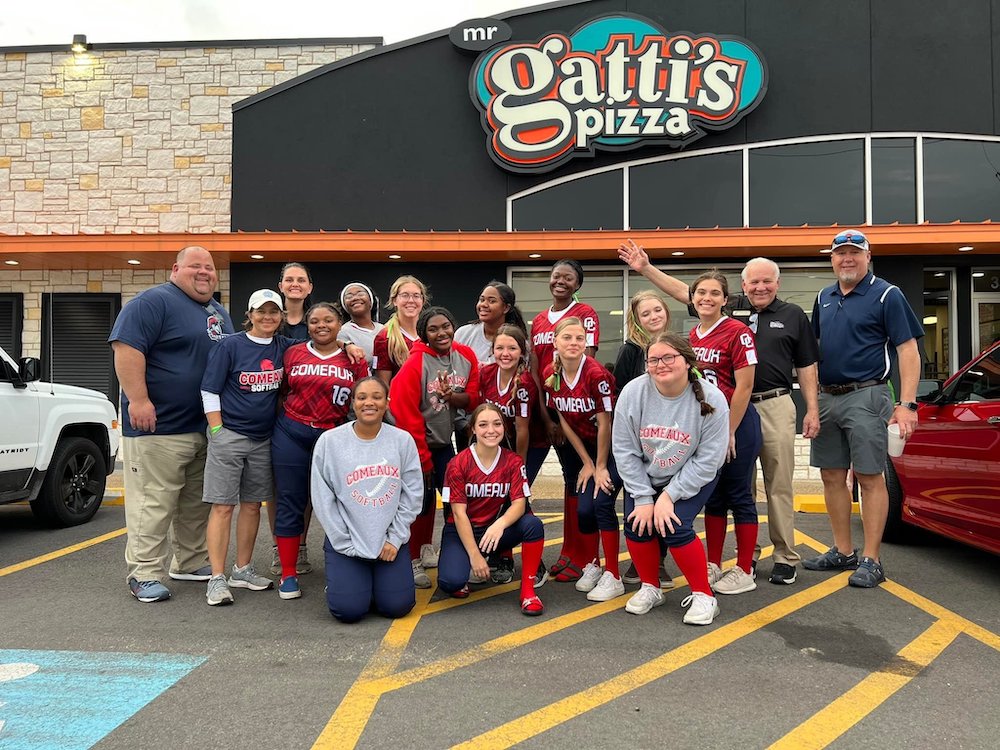 This photo shows a group of young women in softball uniforms posing in front of a Mr Gatti's restaurant