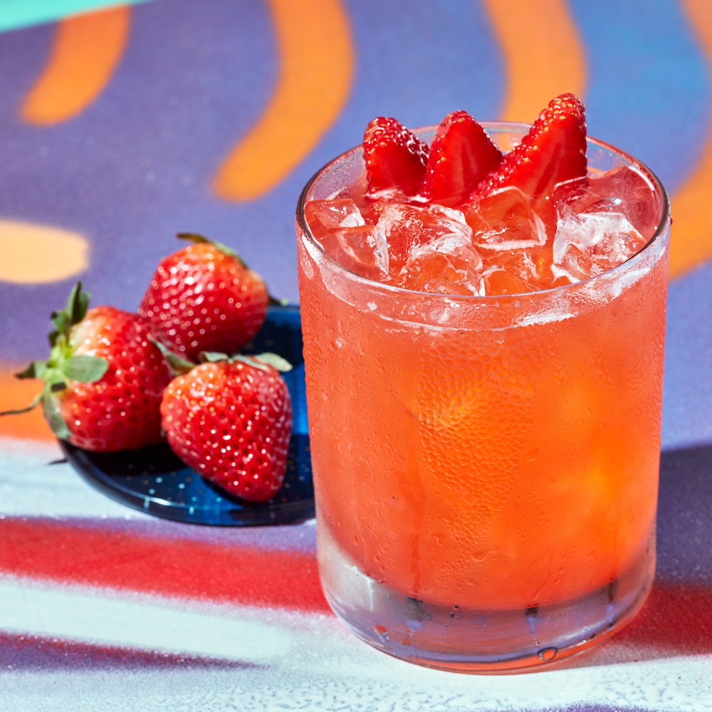 this photo shows the Strawberry Shakedown cocktail, with a small plate of fresh strawberries next to it.