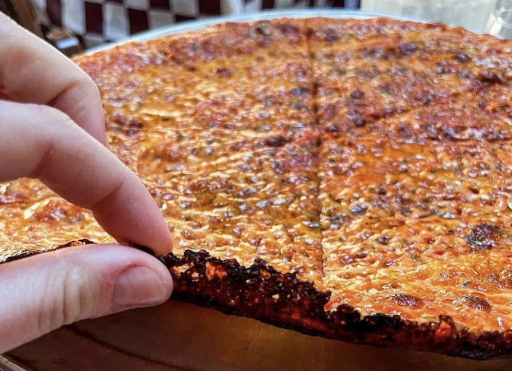 This shows a person's fingers lifting up the crispy, burnt-cheesy crust of the Thinny Thin pizza in close-up