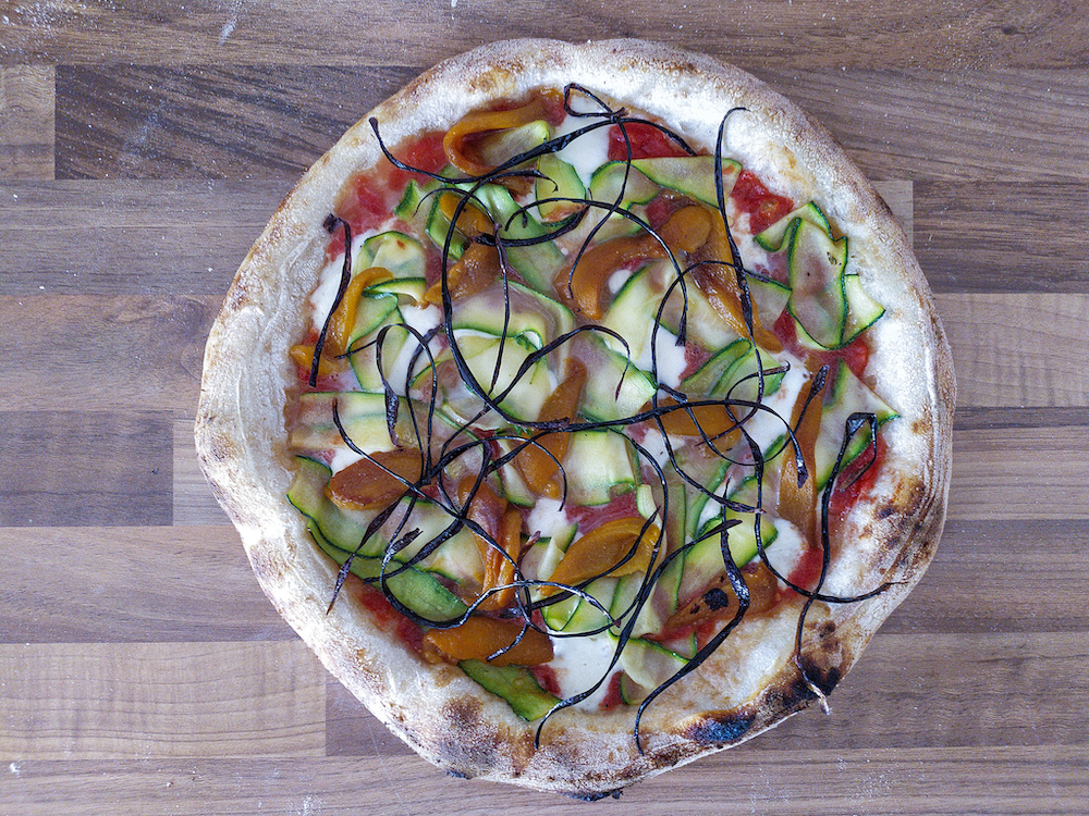 This photo shows an overhead view of a pizza topped with yellow peppers and deep-fried eggplant ribbons.