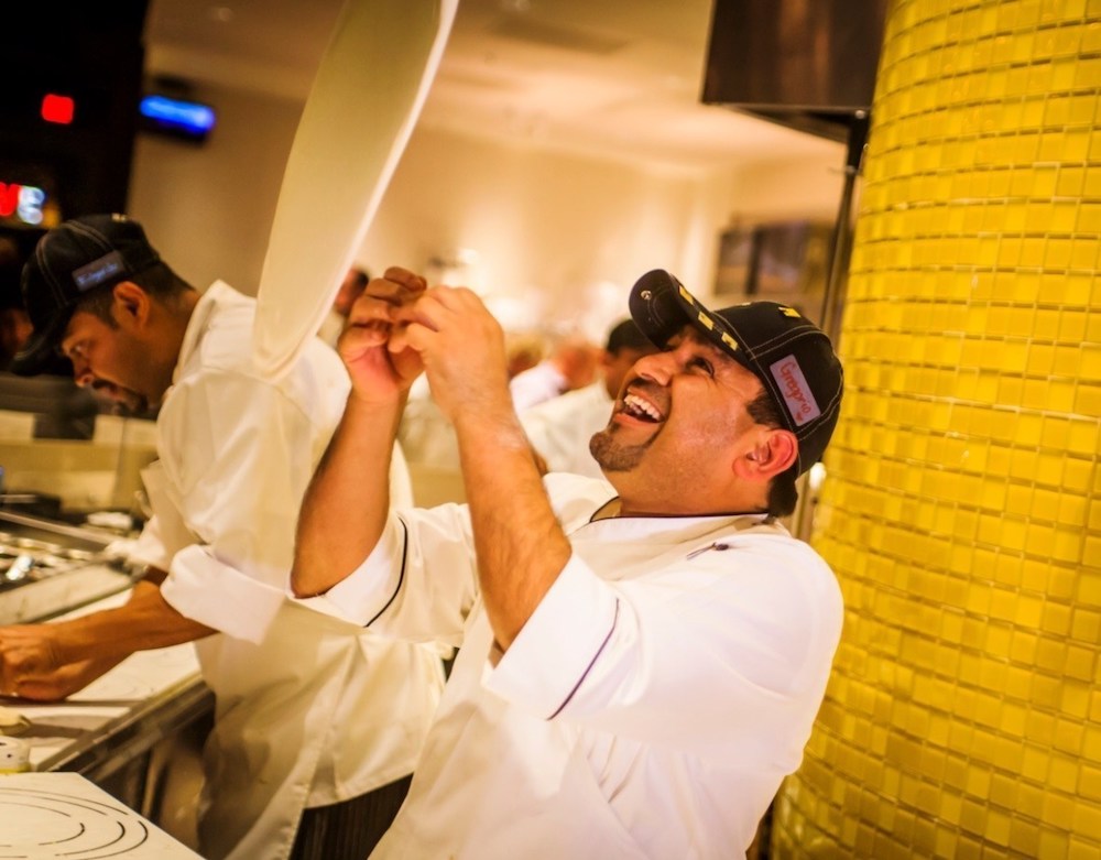 This photo shows a happy-looking pizza chef tossing dough in the air.