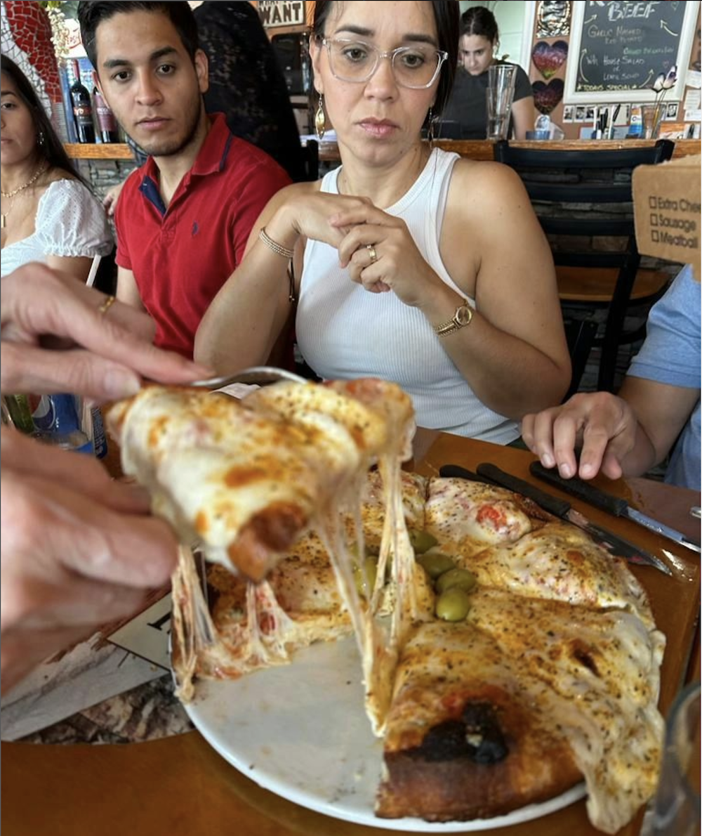 Photo shows a "cheese pull," or a pizza chef lifting a piece of pie with stringy cheese attached.