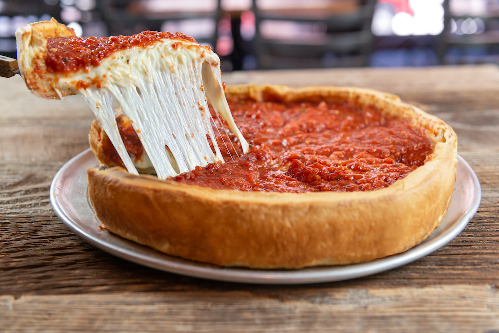 This photo shows a slice of pizza being removed from a Chicago-style deep-dish pizza with a beautiful cheese pull