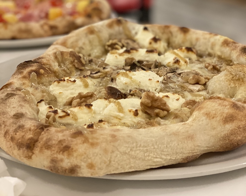 This photo shows a pizza featuring roasted walnuts, walnut puree, sliced mushrooms, fontina cheese, and cream cheese.