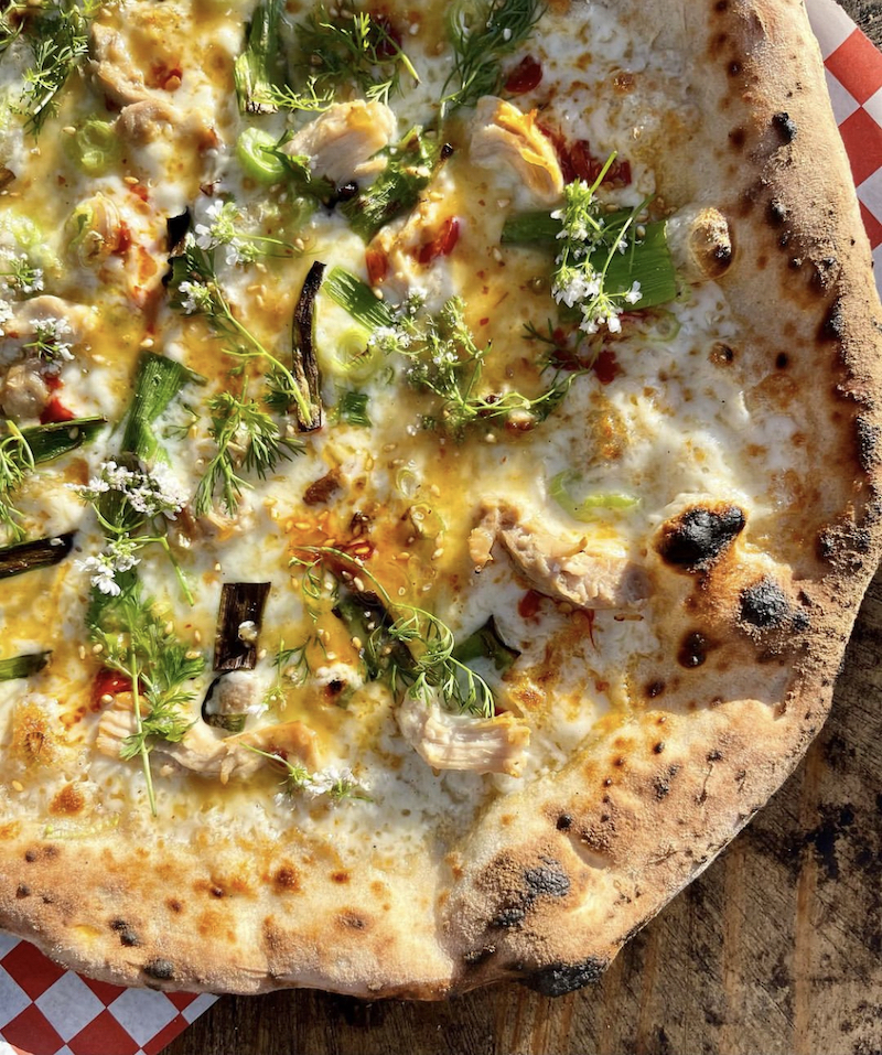 This photo shows a pizza topped with smoked jidori chicken, mozzarella, green onions, Calabrian chilis and a citrus glaze.