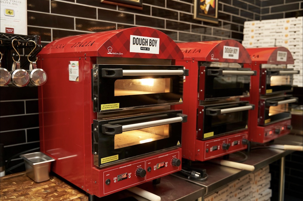 This photo shows a trio of compact fire engine-red pizza ovens with the Dough Boy Pizza logo