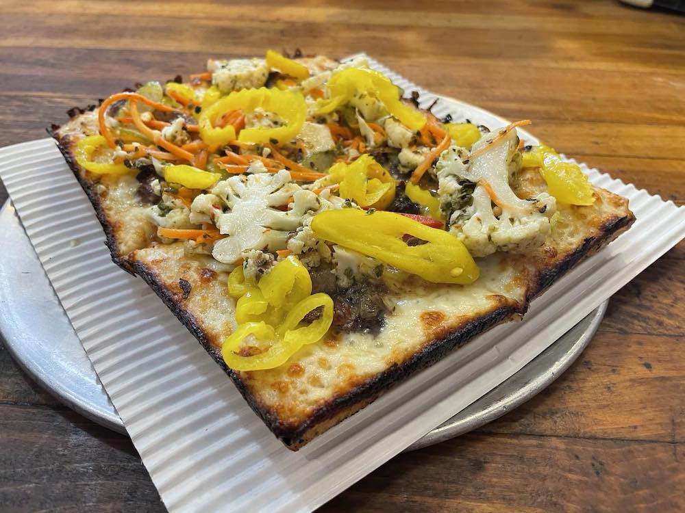 This photo shows a personal-sized square pizza with a nicely crispy edge, topped with pepperoncinis, cauliflower and carrot strips