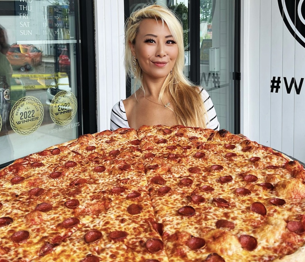 This photo shows Raina Huang grinning as she stands before a gigantic 28-inch pepperoni pizza.