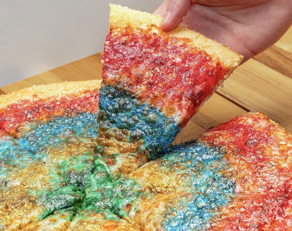 This photo shows a woman's hand removing a slice from a whole pizza that's covered with multi-colored glitter.