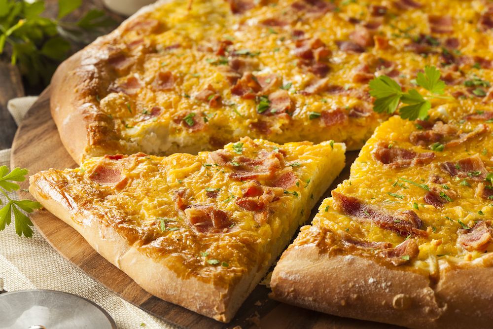 This photo shows a breakfast pizza topped with bacon, eggs and potatoes.