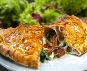 This photo shows a beautiful calzone, sliced in half, with cheese, meat and veggies