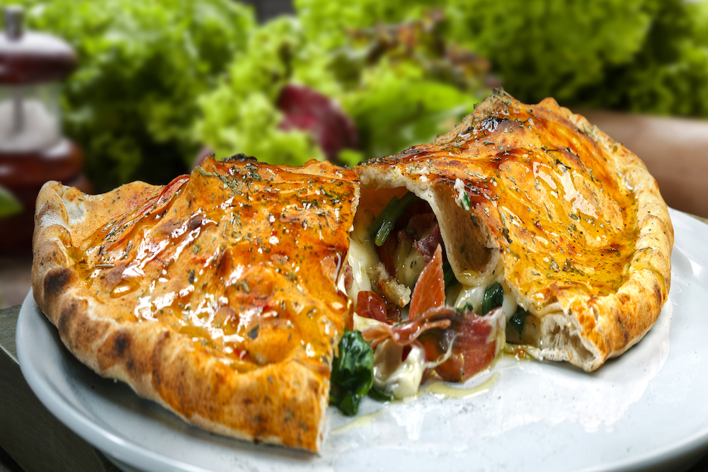 This photo shows a beautiful calzone, sliced in half, with cheese, meat and veggies