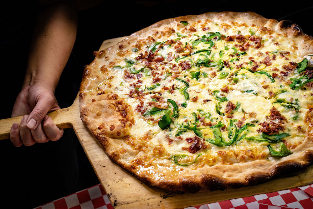 A pizza maker holds a finished pie on a pizza peel.