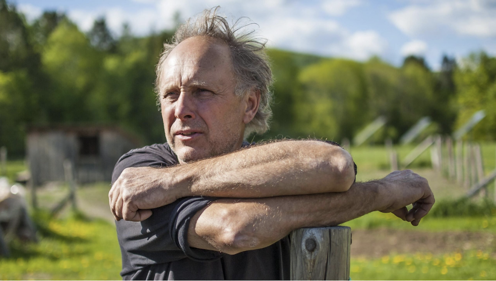 George Schenk, founder of American Flatbread, stands against a fencepost in a New England field.