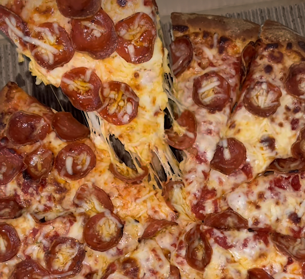 This photo shows a slice being pulled out of a whole pie topped with pepperoni and spicy-hot cheese.