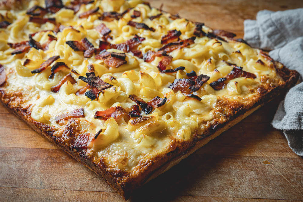 This photo shows a Detroit-style pizza topped with macaroni and cheese and bacon.