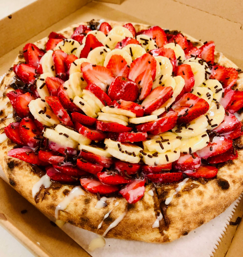 This photo shows a dessert pizza topped with Nutella, strawberries and bananas