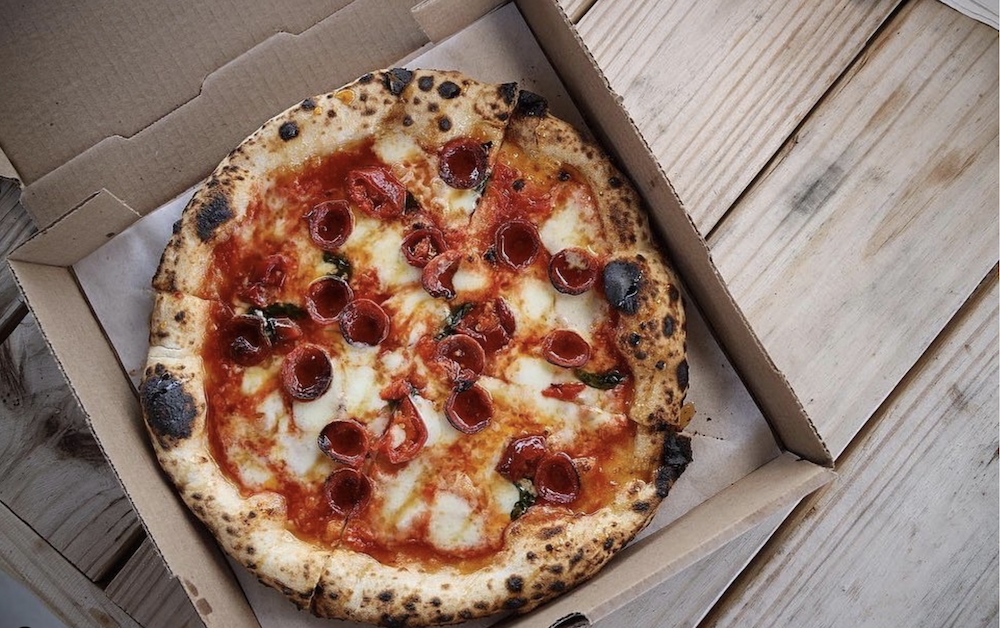 Photo shows a Pepperoni Pizza in a box on a picnic table.
