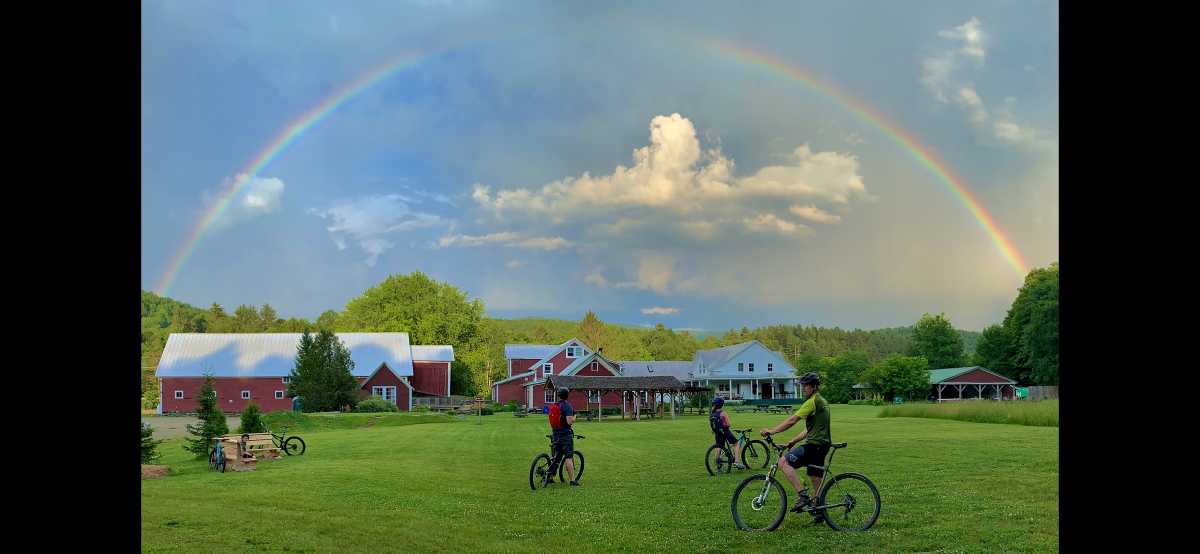 A photo of American Flatbread at Lareau Farm in Waitsfield, Vermont, with a rainbow over the beautiful New England field.