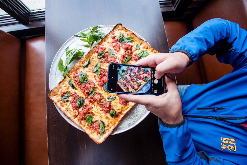 This photo shows Jim Mirabelli's hands shooting a photo of a beautiful Margherita pizza with his smartphone.
