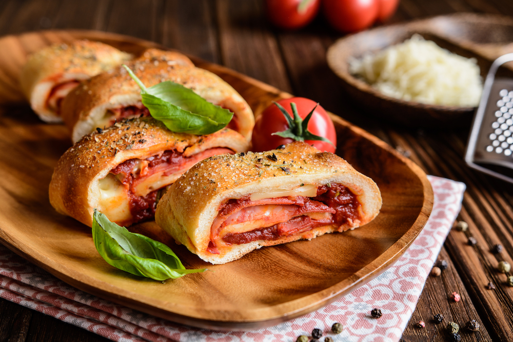 This photo shows a Traditional Italian Stromboli stuffed with cheese, salami, green onion and tomato sauce