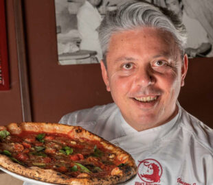 This photo shows Vincenzo Esposito, with swept back graying hair, holding one of his famous Margherita pizzas.