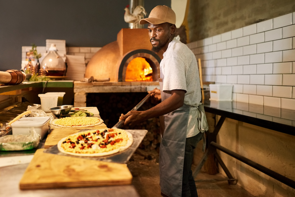 Chef making pizzas in a commercial kitchen. Cook making pizza at a restaurant and grabbing it to put it in the oven.