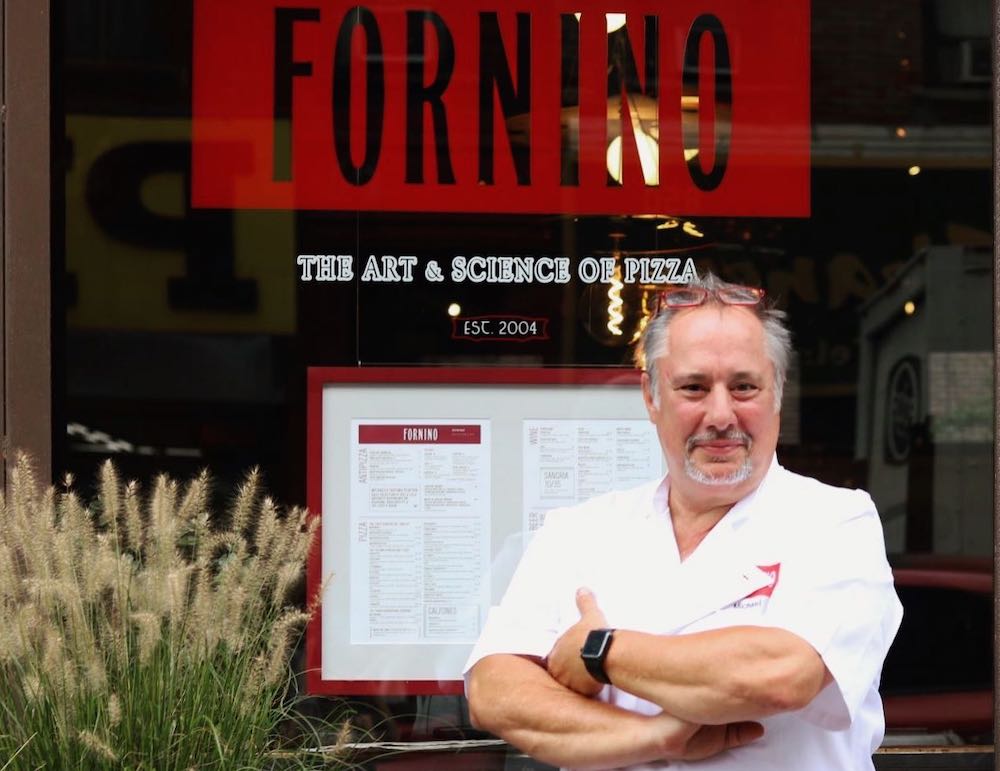 This photo shows Chef Michael Ayoub, arms folded and wearing a white chef's shirt, standing outside his pizzeria with the Fornino sign right behind him.