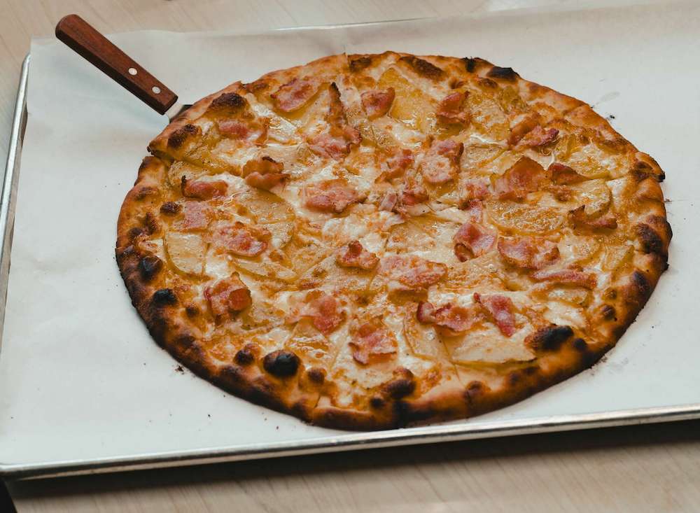 This photo shows the Patata Rustica, a pizza topped with gold potatoes, bacon and three cheeses.