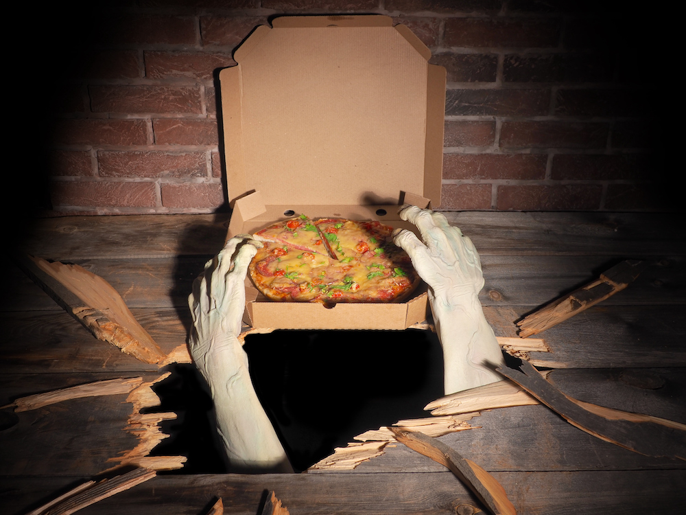 This photo shows a pair of ghostly-white, zombie-like hands reaching through cracked wood to grab a pizza.