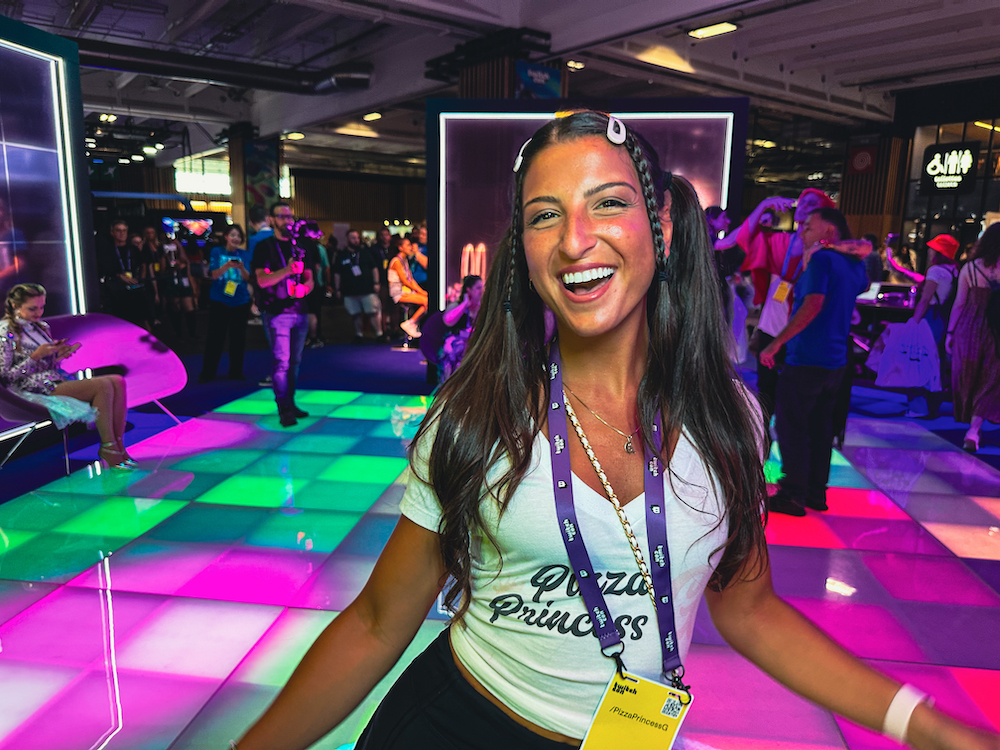 This photo shows Giuliana, wearing a white t-shirt that reads Pizza Princess G, standing in the colorfully lit facility where Twitch Con is taking place.