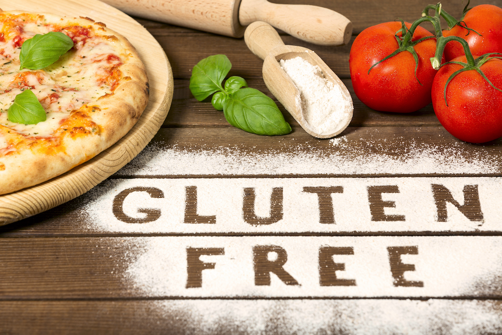 A gluten free pizza on a rustic wood background, with word " gluten free" made of flour, tomato, basil, spoon of flour.