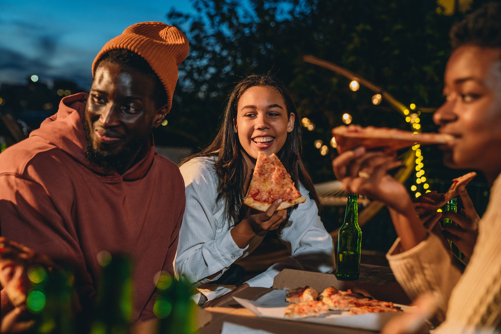 Friends are dining together with pizza. They are at a dinner party on a rooftop.